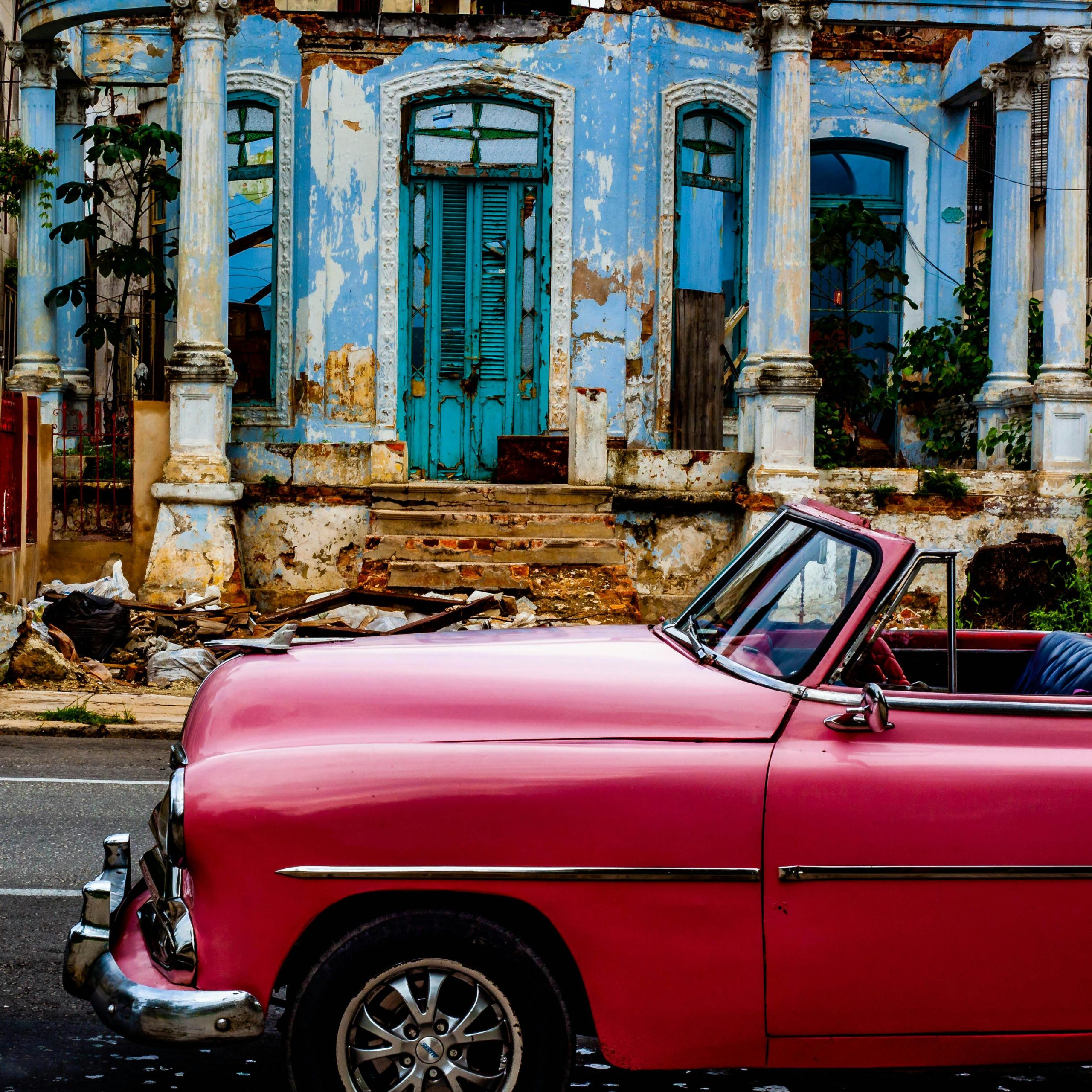 A classic pink car parked by a weathered building in Havana, exhibiting nostalgic urban charm.
